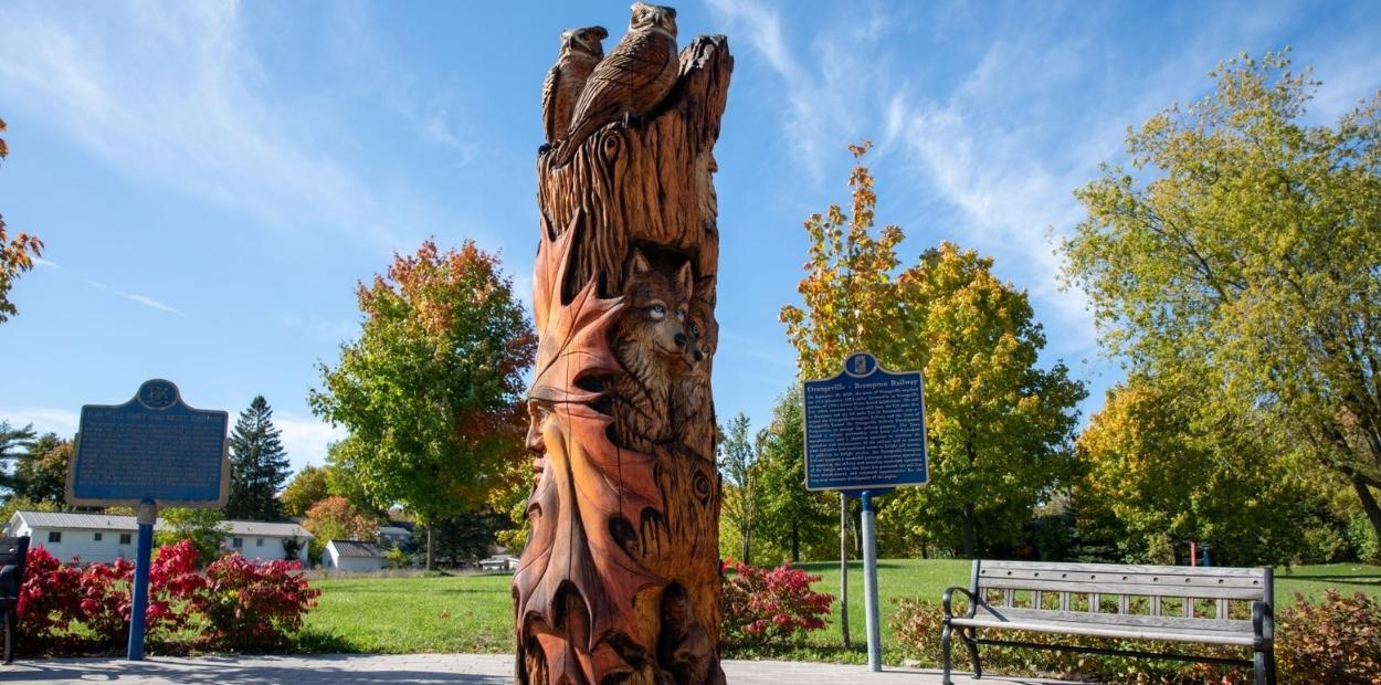 A tree trunk carved with different animals into it - wolf faces, wooden birds are perched on top and a human face into a giant leaf. The titled of the tree sculpture is Nature's Unity. 